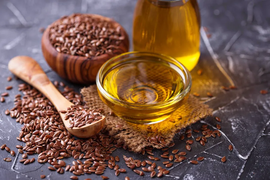 Flaxseed oil in a small glass bowl with flaxseed on a wooden spoon beside it 
