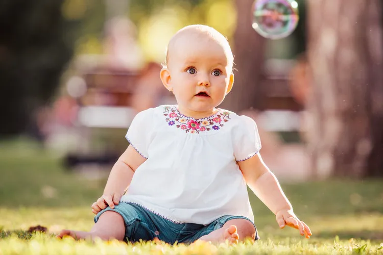 Baby sitting in the park staring at a bubble