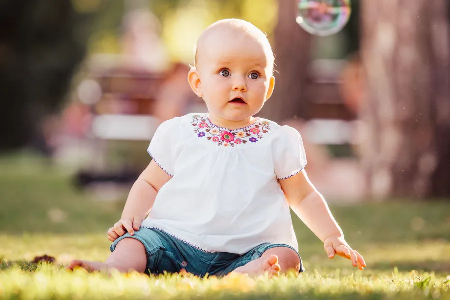 Baby sitting in the park staring at a bubble