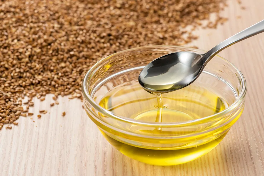 Flaxseed Oil in a small glass bowl with Flaxseed in a pile behind
