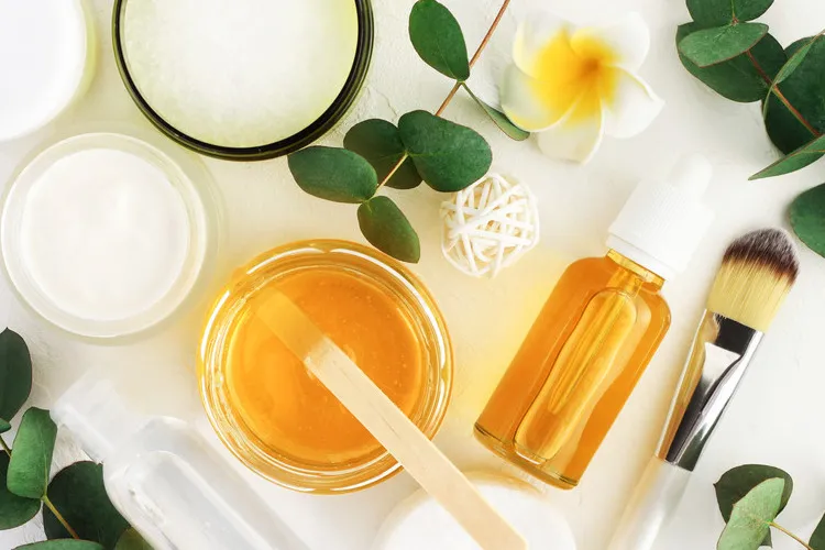 Mānuka honey skincare ingredients with a jar of golden honey, serum dropper bottle, face creams, brush and natural botanicals.