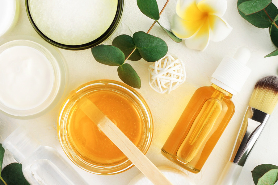 Mānuka honey skincare ingredients with a jar of golden honey, serum dropper bottle, face creams, brush and natural botanicals.