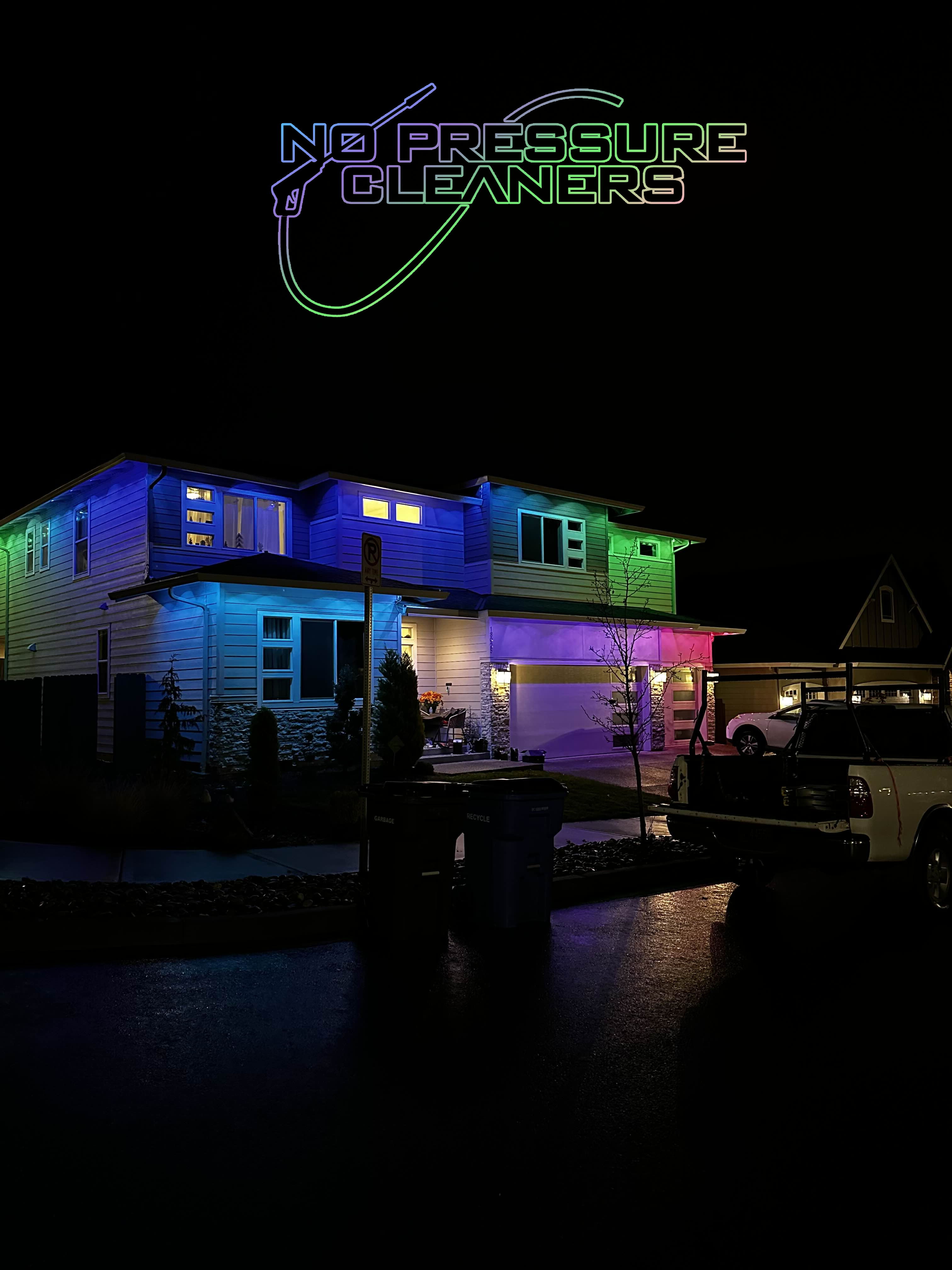 Two-story house at night illuminated with colorful blue, purple, green, and pink exterior lights, with vehicles parked on the street and a 'No Pressure Cleaners' logo above.