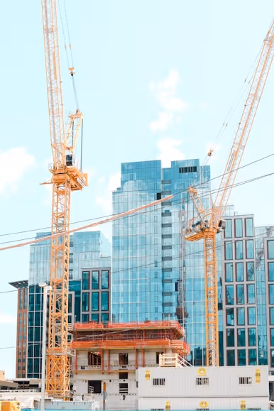Construction site with cranes and modern buildings against a blue sky.