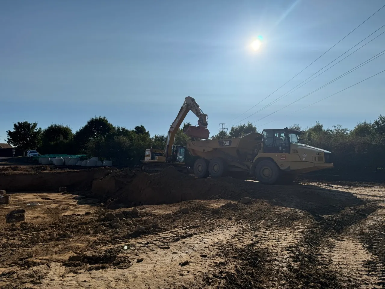 Stavební stroj nakládá zeminu do nákladního auta na staveništi za jasného slunečného dne.