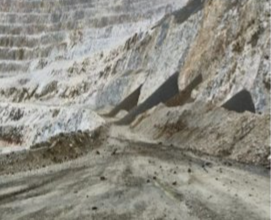 Steep, terraced rock face with a dirt path below, possibly a quarry or open-pit mine.