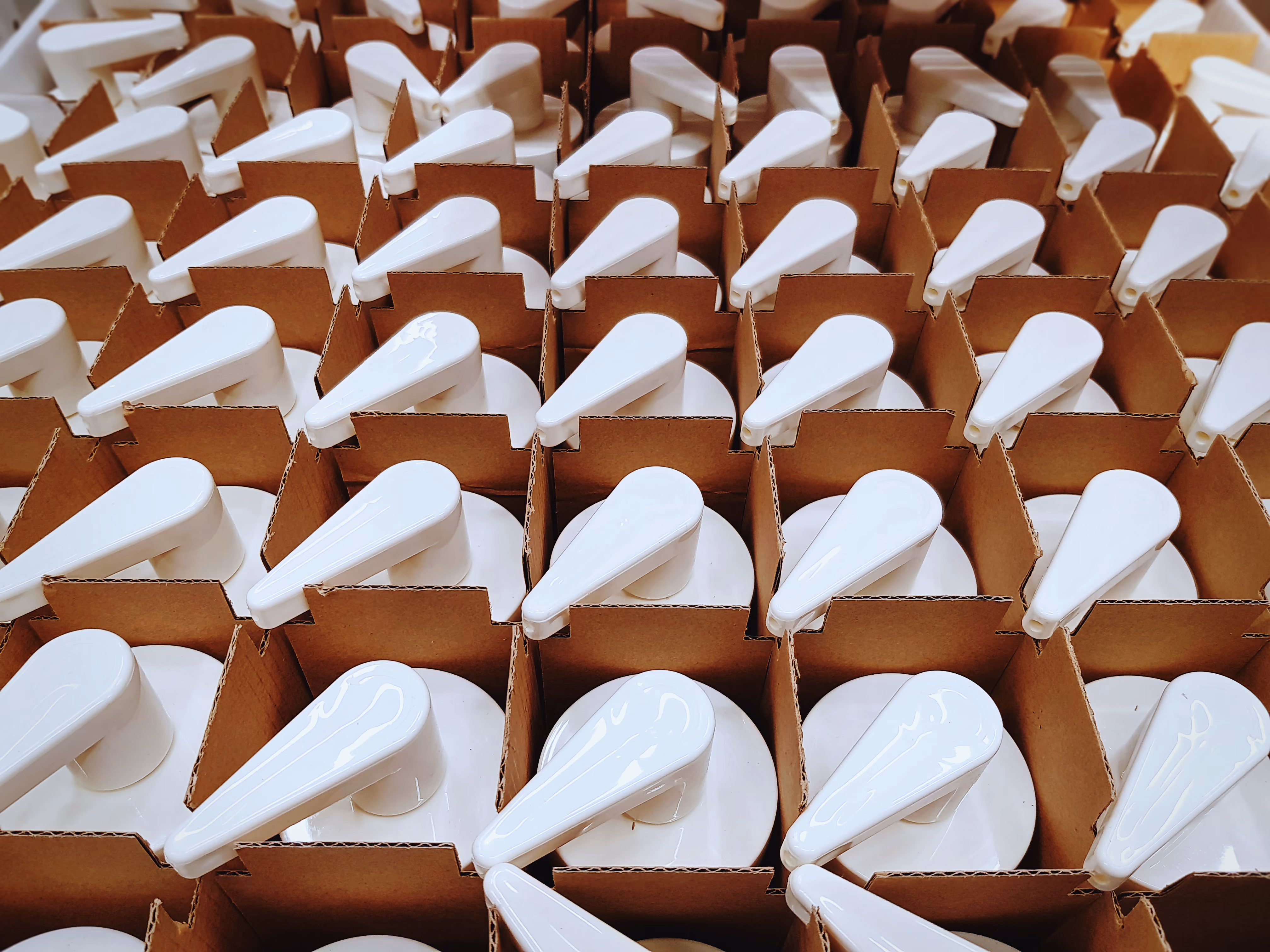 Rows of white plastic pump dispensers neatly arranged in a grid inside brown cardboard packaging.