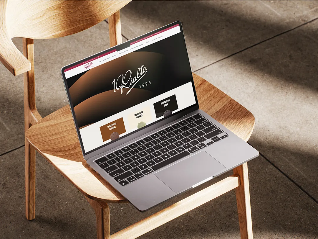 Portátil abierto mostrando el sitio web de 100 Rialto sobre una silla de madera clara.