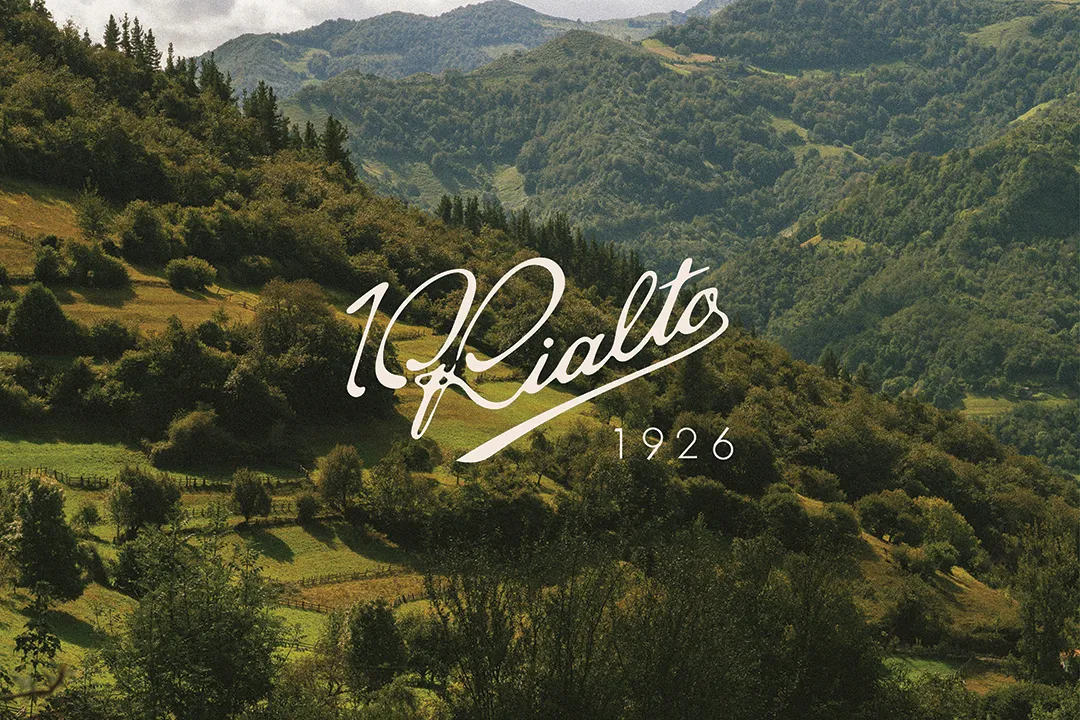 Paisaje montañoso con árboles y praderas verdes, sobre el que aparece el texto '100 Rialto 1926' en estilo manuscrito.