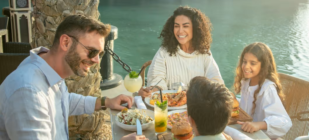 A happy family enjoying a sunny outdoor meal by the water.