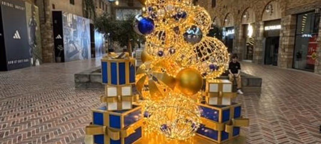A festive outdoor display of large golden light spheres and blue gift boxes in a stone plaza