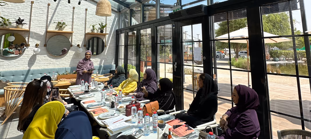 A group of women in abayas gathered for a meeting or social event at a bright, modern restaurant
