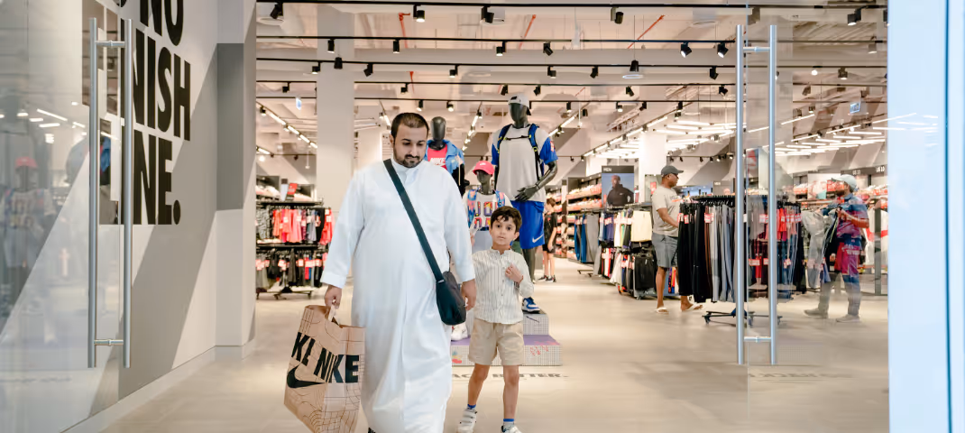 A man and child walking through a brightly lit Nike retail store with shopping bags.