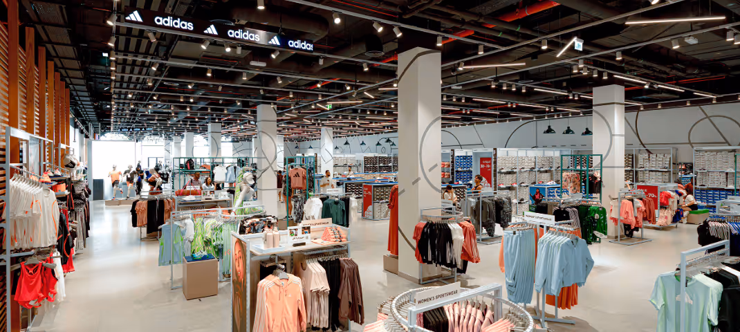 A spacious, brightly lit Adidas retail store filled with racks of colorful athletic apparel.