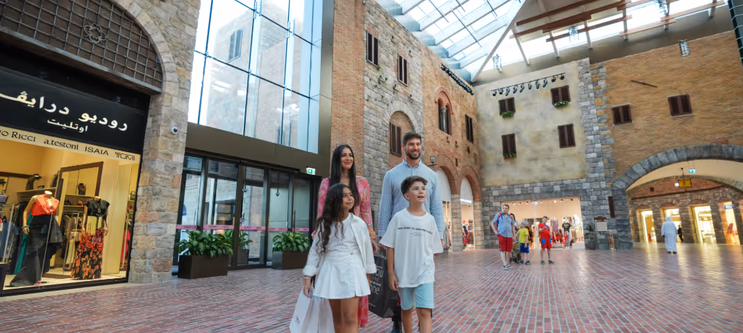 A family walks through an indoor mall designed with rustic, European-style brick architecture.