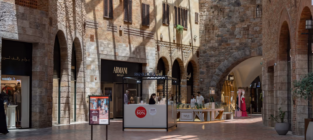 Upscale shopping outlet with stone arches featuring Armani and Pandora storefronts.