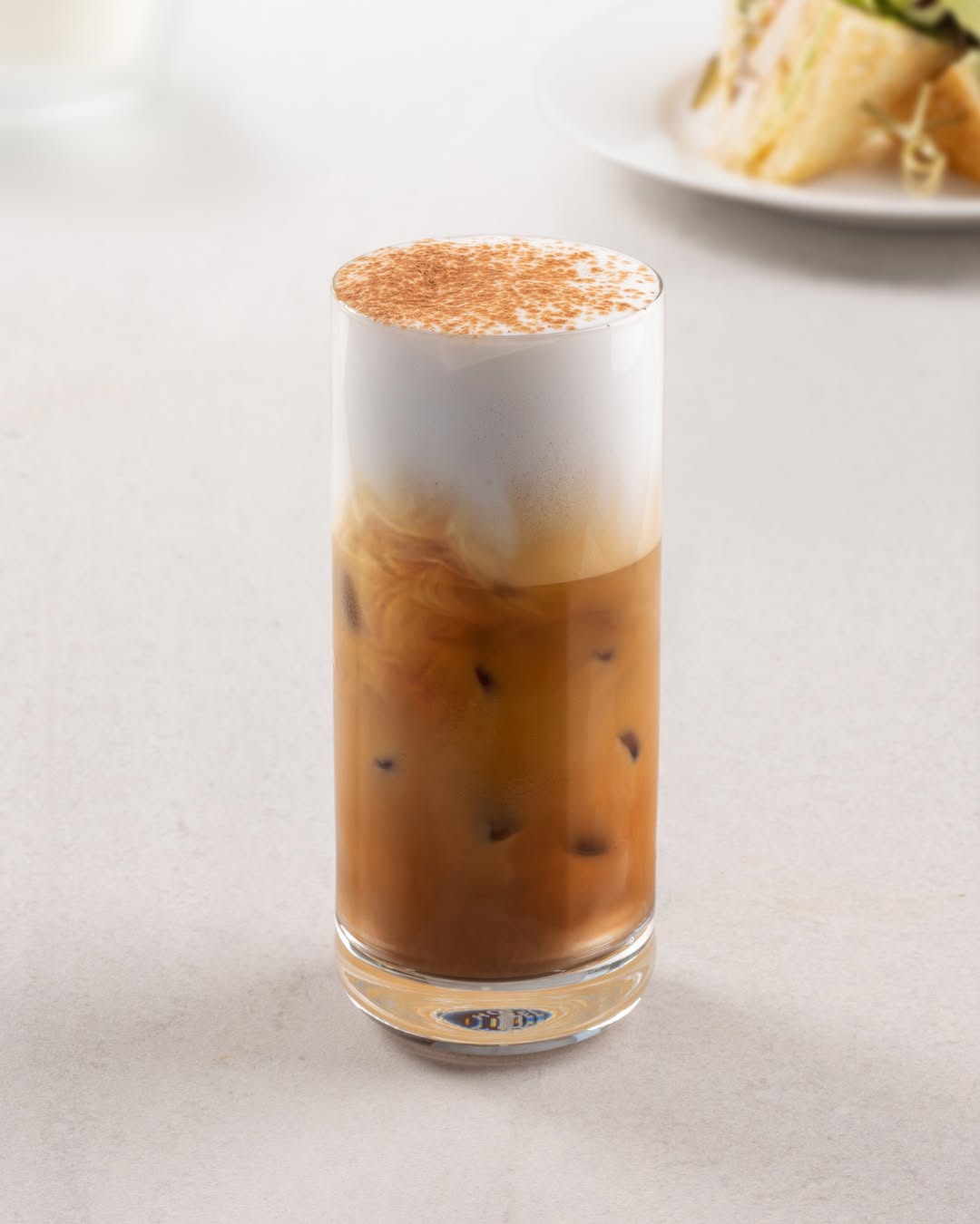 An iced coffee with a thick layer of foam and a dusting of cinnamon on top