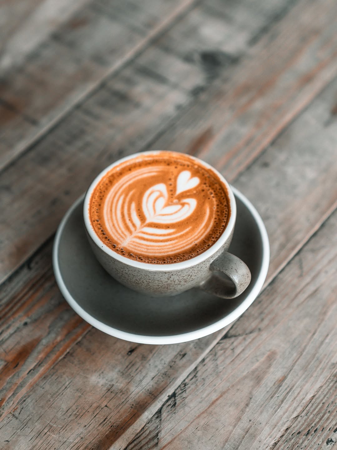 A gray ceramic cup of latte with heart-shaped foam art sits on a rustic wooden table.