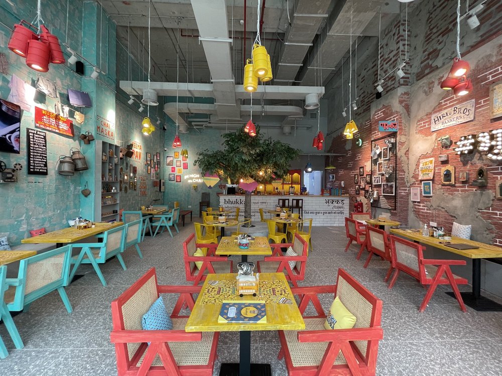 Vibrant cafe interior with teal and brick walls, colorful chairs, and unique hanging light fixtures.
