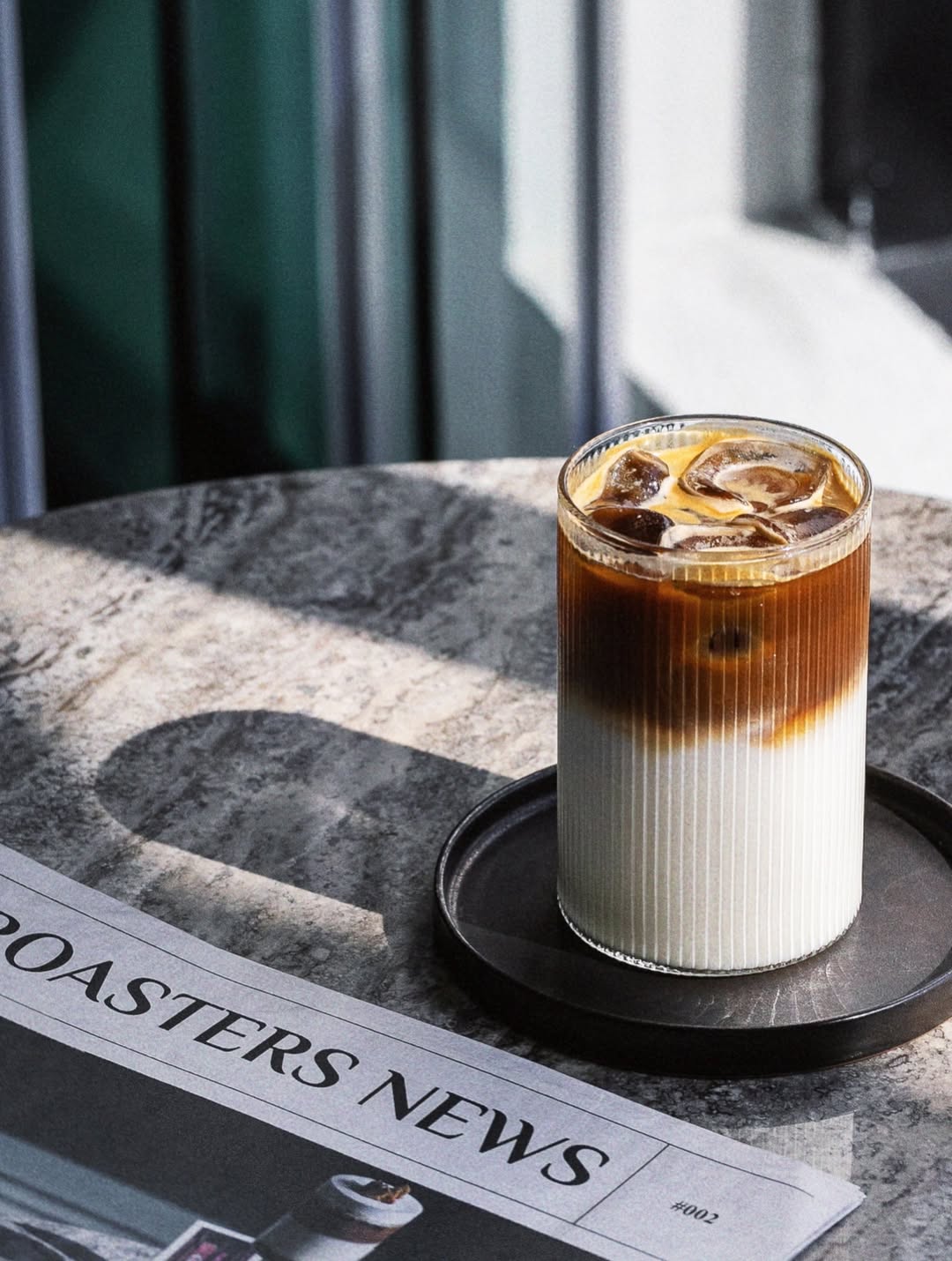 Layered iced coffee in a ribbed glass on a marble table next to a newspaper