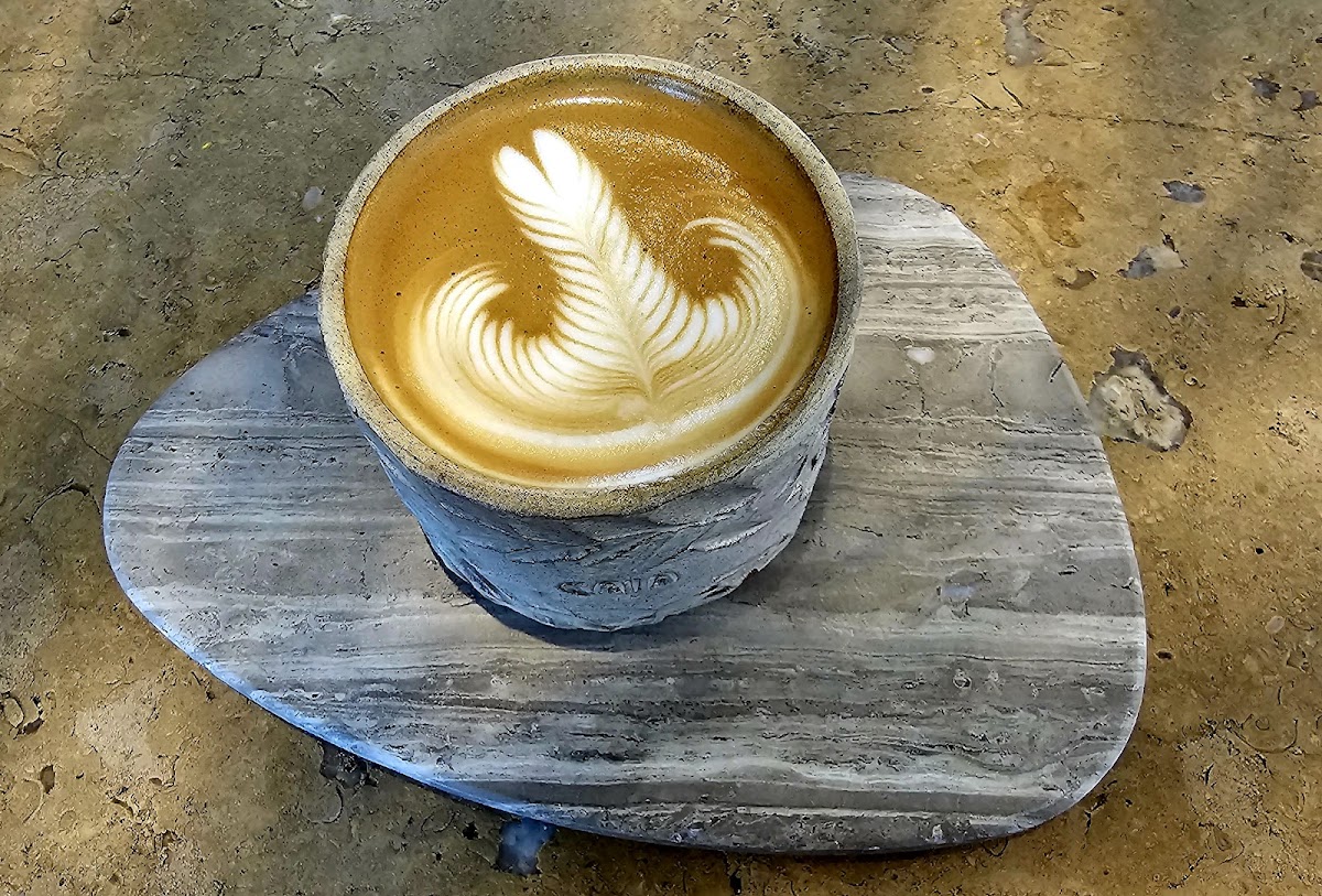 A stone-textured cup of latte with feather latte art on a triangular stone coaster.