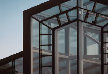 A glass structure with a dark frame shows reflections under a clear sky.