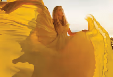 A woman in a flowing, sunlit yellow dress twirling gracefully in a bright setting.