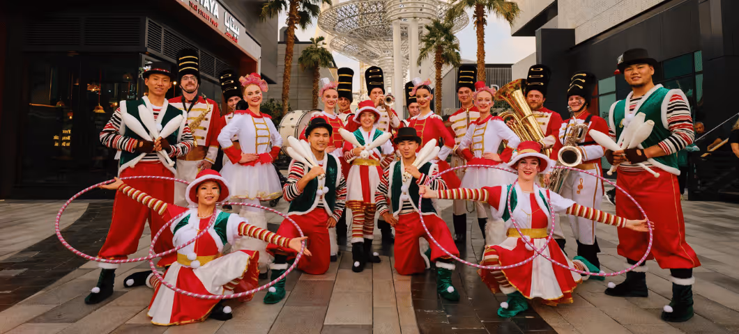 Performers in festive red and green costumes posing in a plaza, featuring a girl with hula hoops