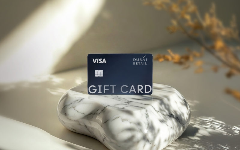 Dubai Retail Visa Gift Card displayed upright on a white marble pedestal with soft natural lighting and blurred decorative foliage in the background.