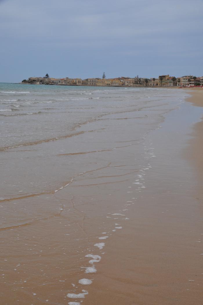 A sandy beach with buildings in the backgroundAI-generated content may be incorrect.