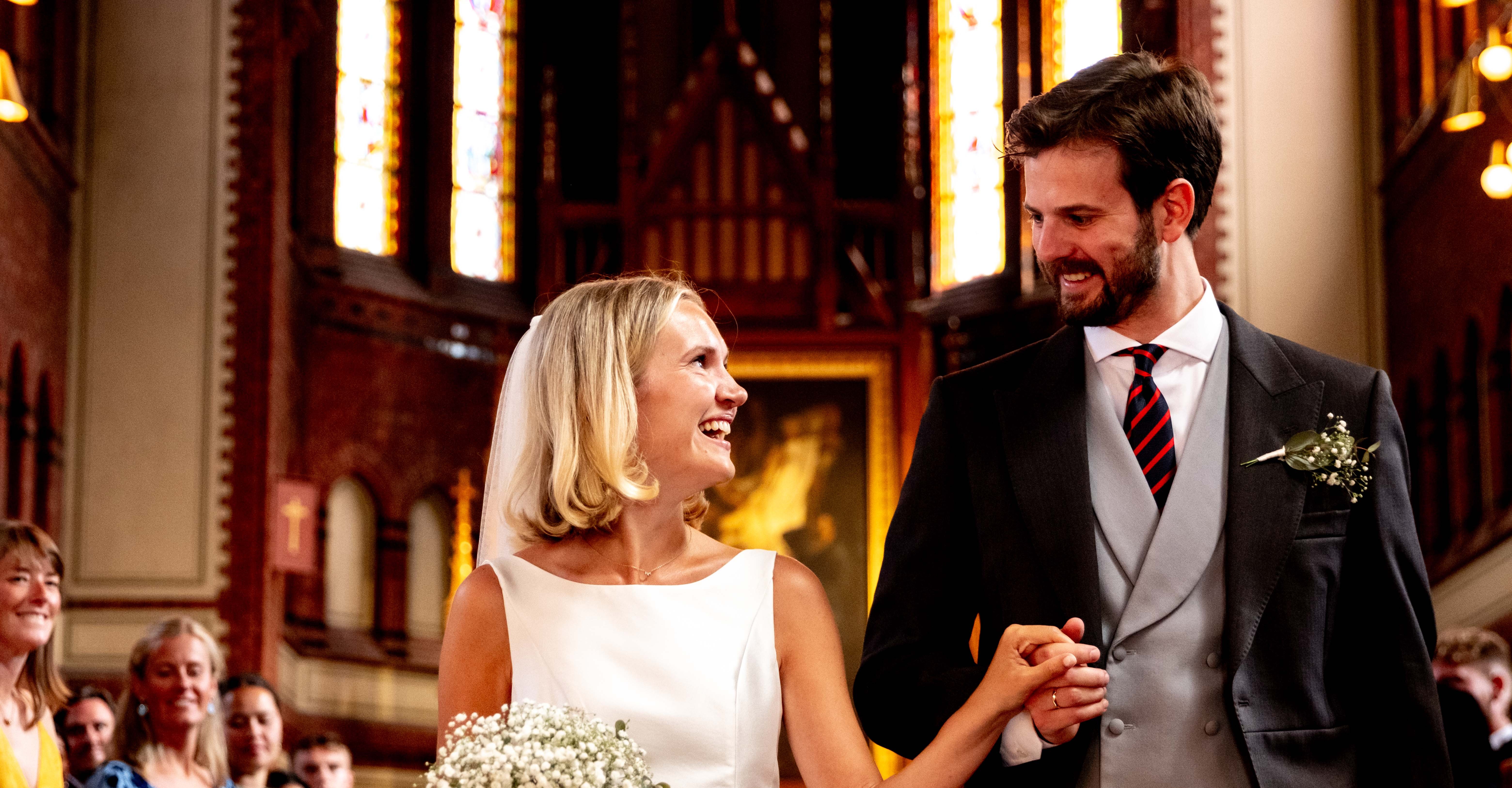 Bride and groom smiling at each other holding hands inside a church during their wedding ceremony.