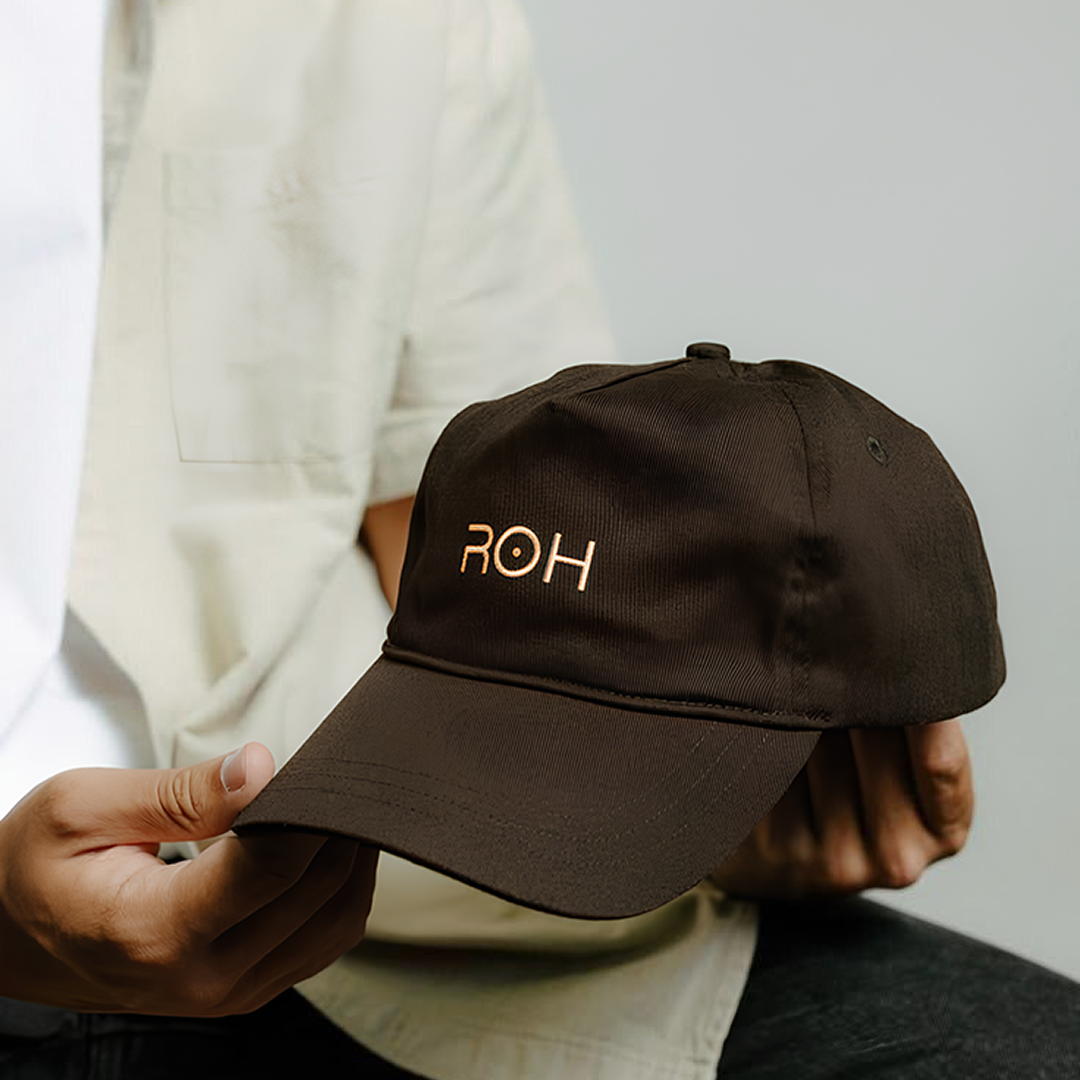 Person holding a brown baseball cap with the ROH lgoo embroidered on the front.