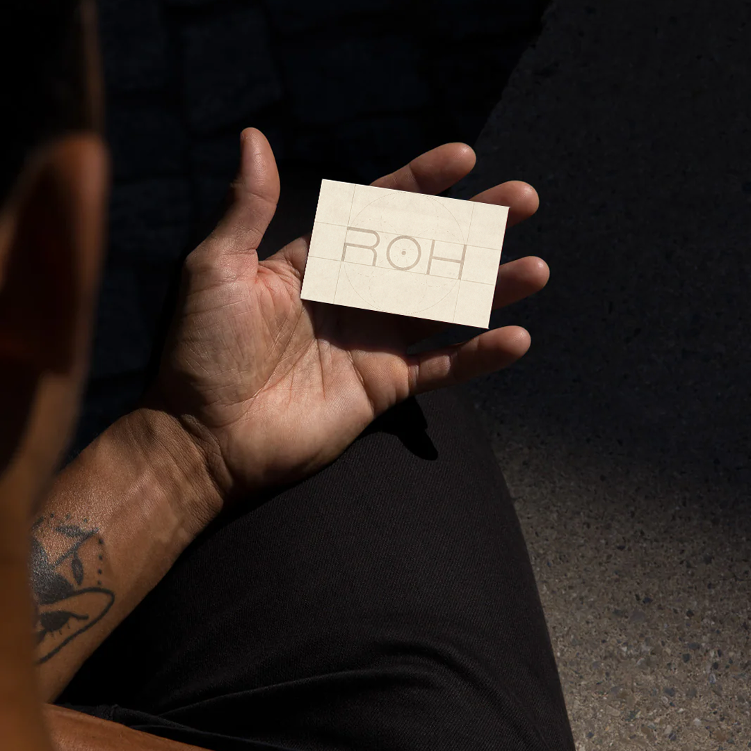 Person holding a business card with the ROH Logotype on it in their left hand