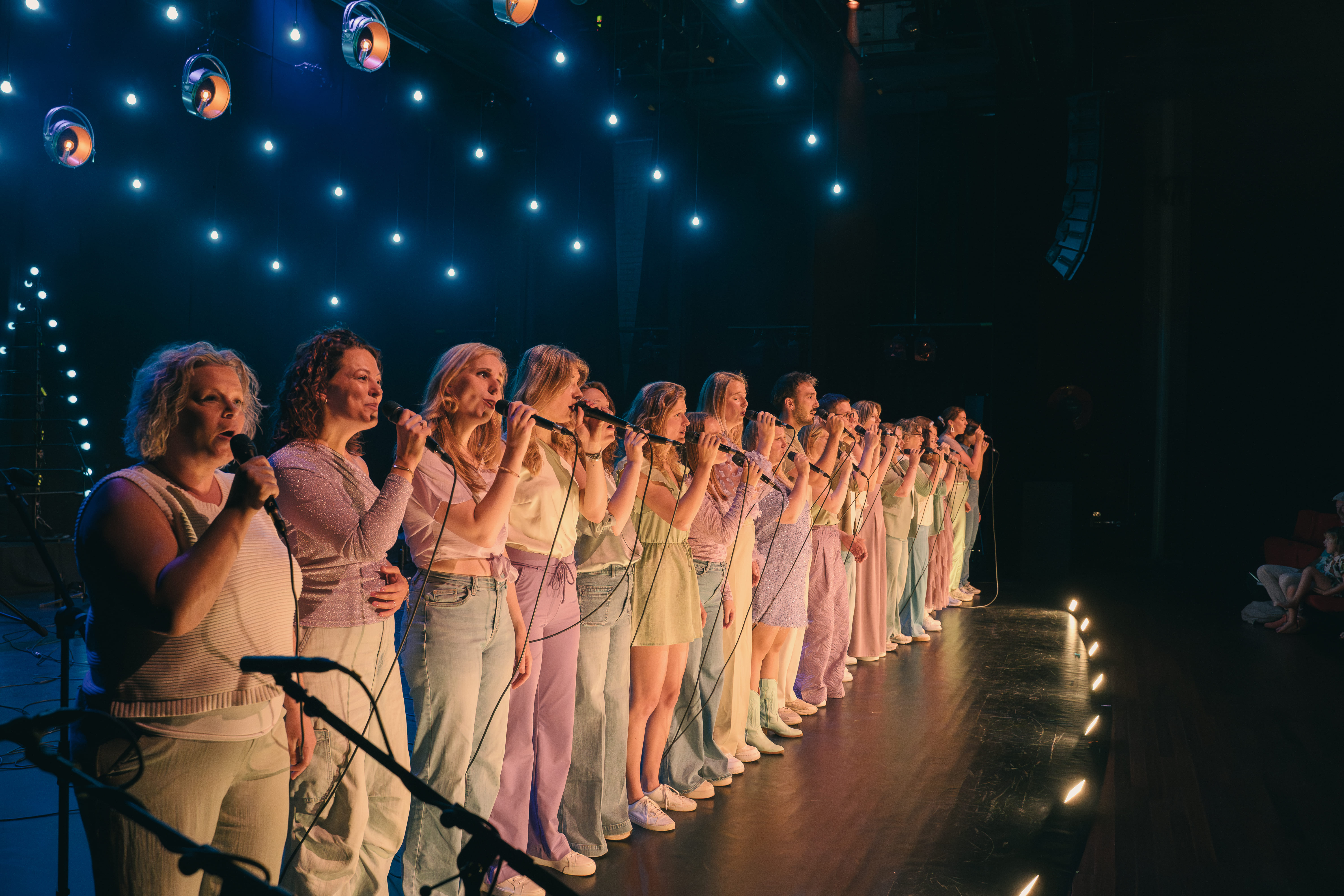 Rij zangers met handmicrofoons op een theaterpodium