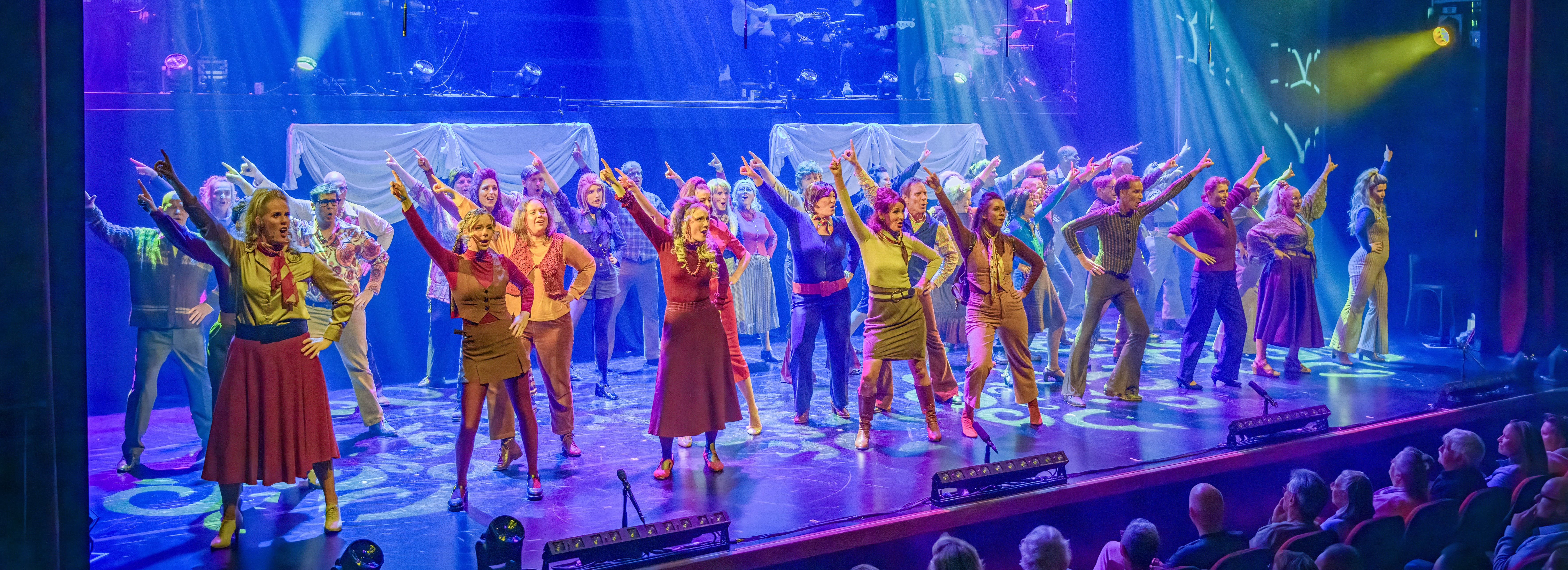 Volledige cast op een theaterpodium in kleurrijk licht
