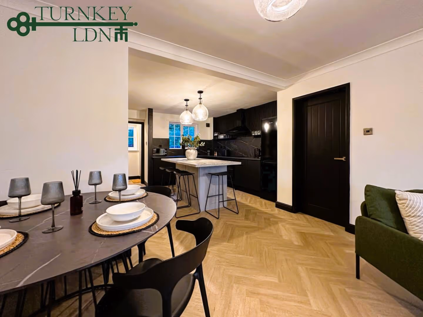 Modern open kitchen and dining area with black furniture, marble-topped island, and wood-patterned floor.