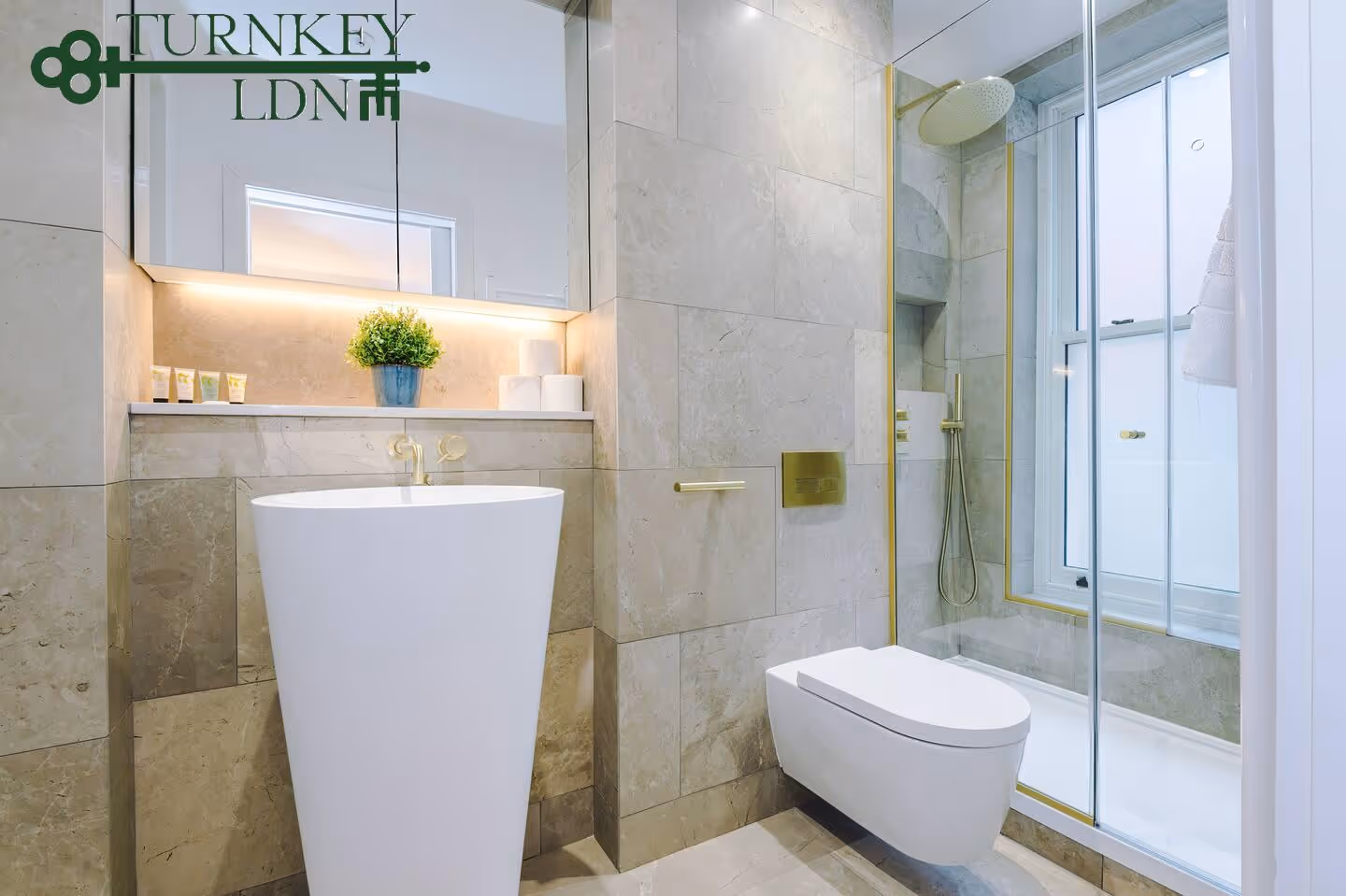 Modern bathroom with a freestanding white sink, wall-mounted toilet, glass-enclosed shower, and beige marble tiled walls.