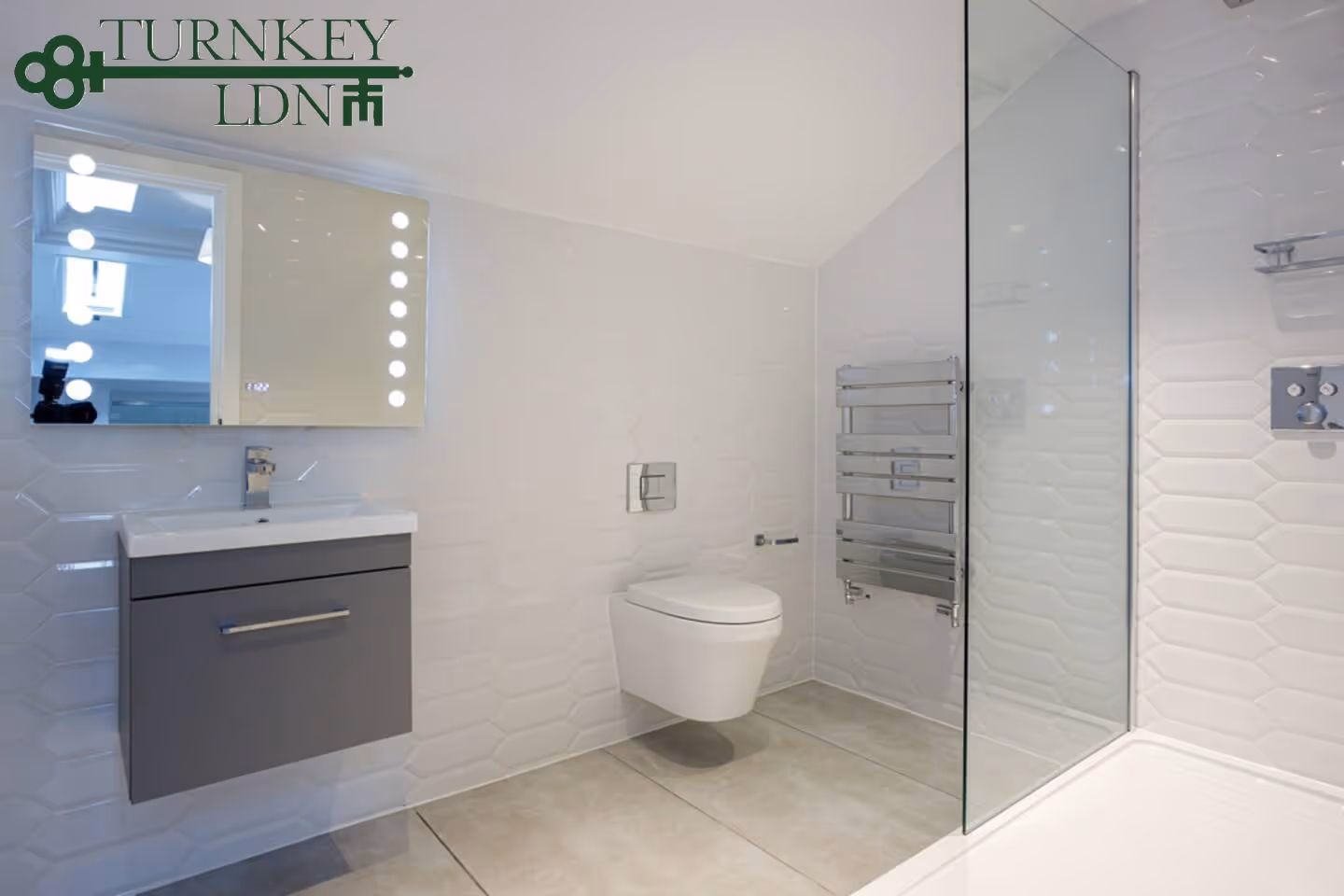 Modern bathroom with wall-mounted toilet, gray floating vanity with sink and illuminated mirror, glass shower partition, and chrome towel radiator.