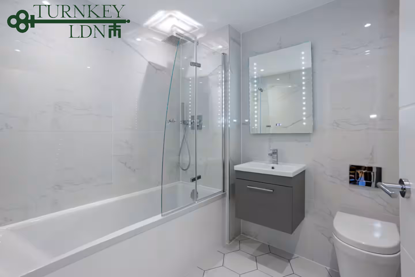 Modern bathroom with white bathtub, glass shower screen, gray floating vanity with mirror, and toilet.