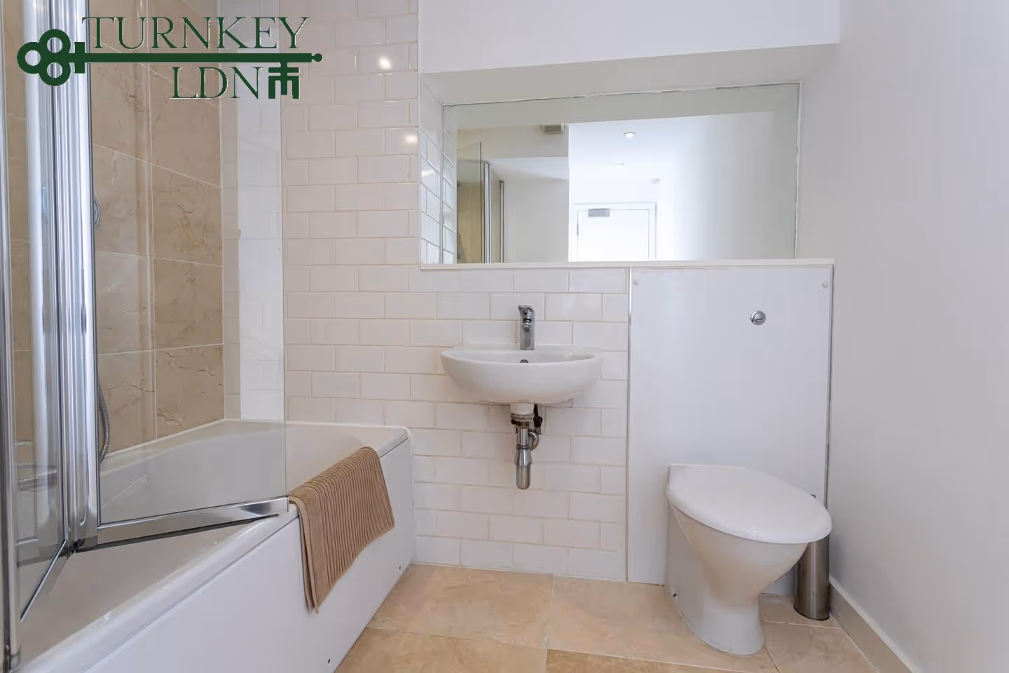 Minimalist bathroom with a white bathtub and glass shower screen, a wall-mounted sink, and a toilet with a concealed cistern.