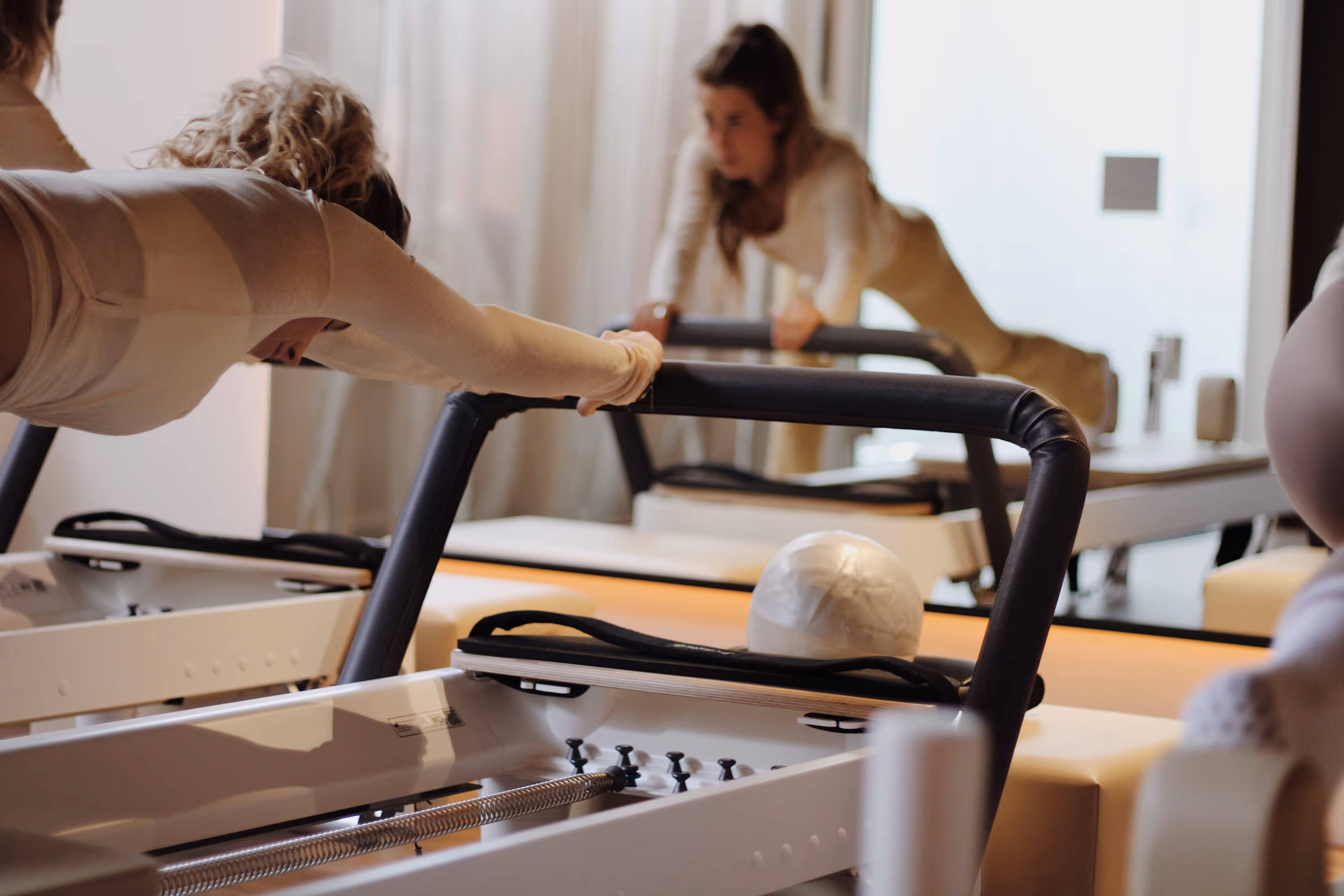 Twee vrouwen doen reformed pilates oefeningen op pilates reformers in een lichte studio.