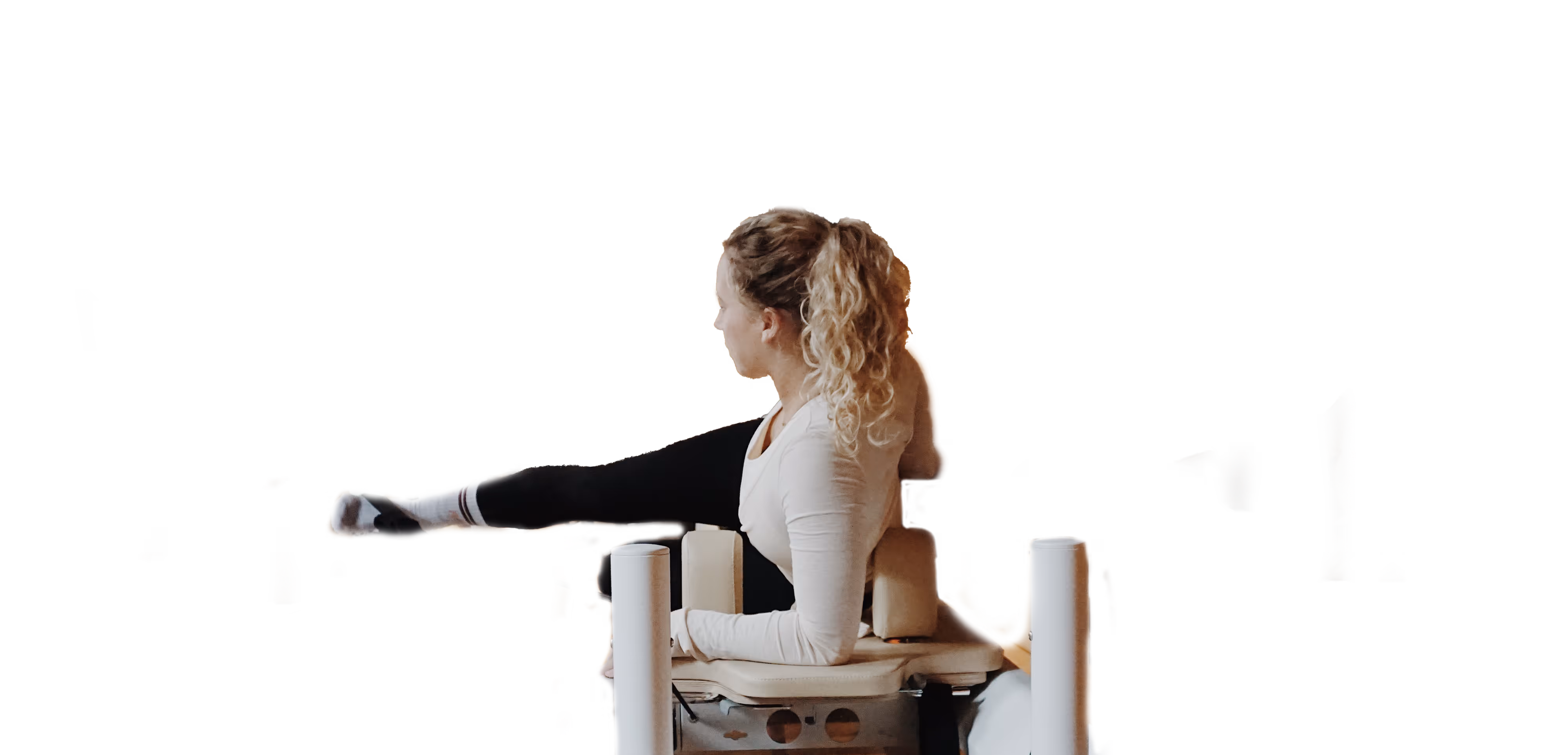 Vrouw rekt haar been uit terwijl ze op een Pilates-apparaat zit.