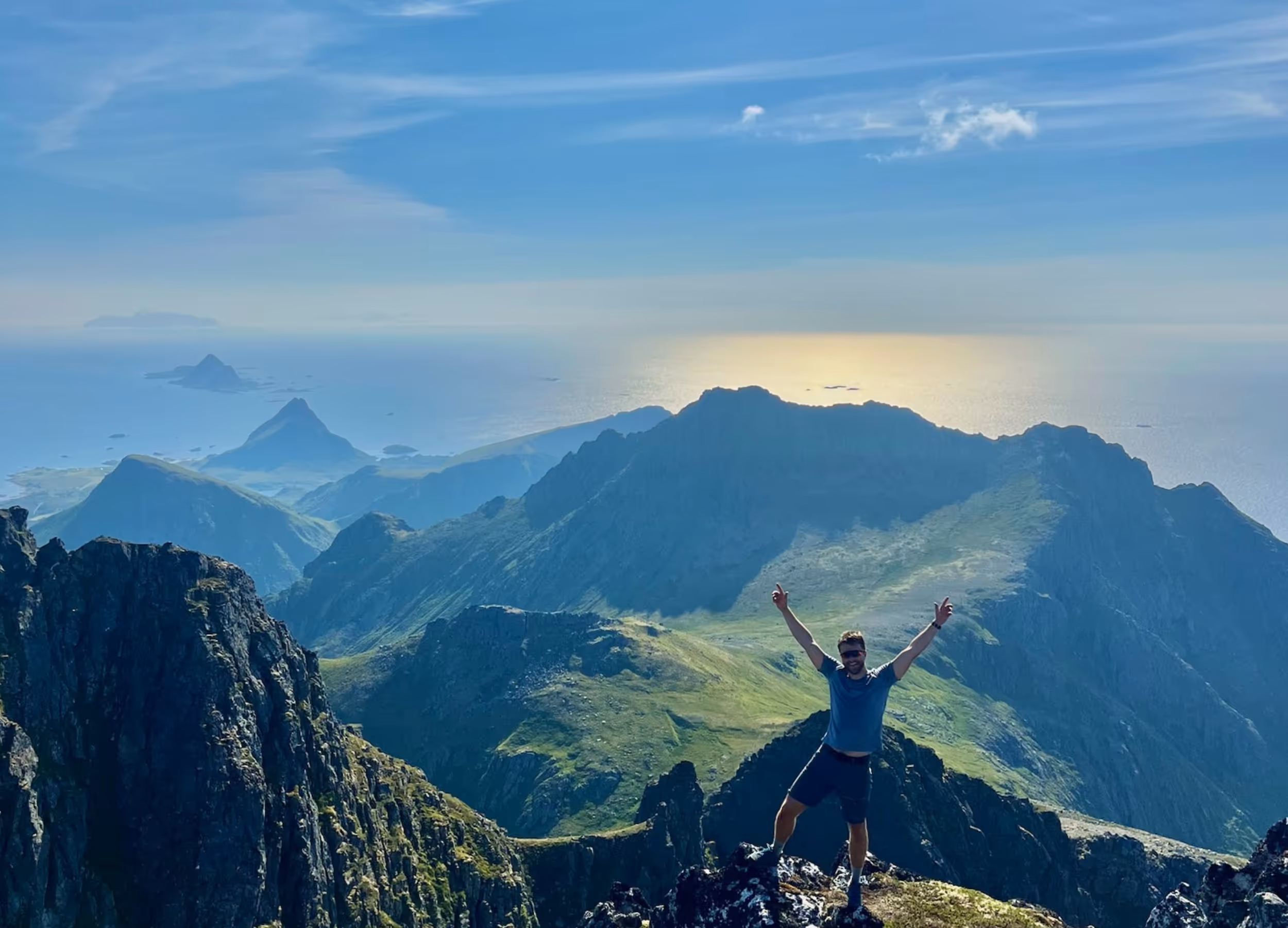 Person på fjelltopp i Vesterålen med utsikt over dramatiske fjell og hav – ekte nordnorsk frihet.