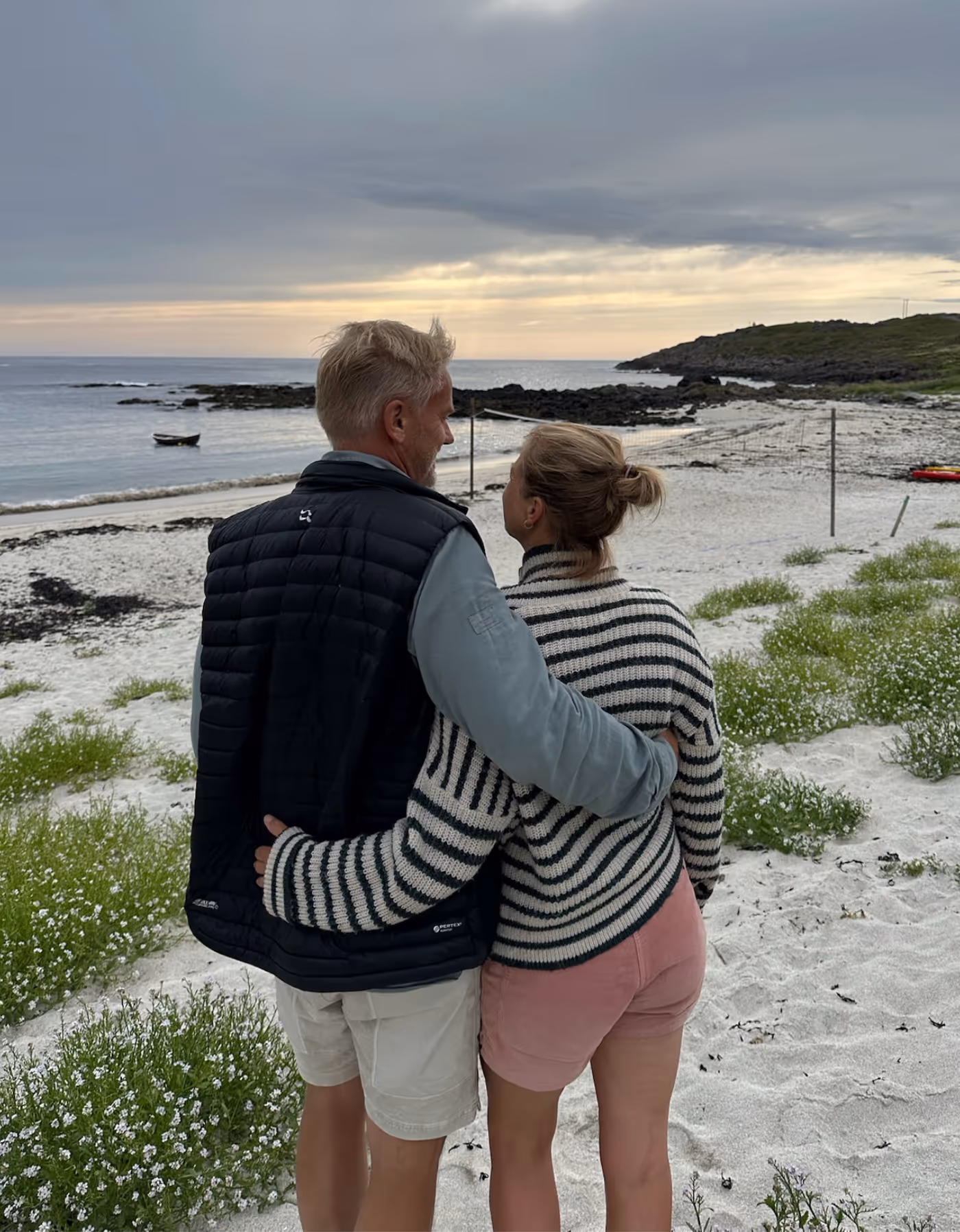 En mann og en kvinne står med ryggen til og holder rundt hverandre, med utsikt over stranden i Vesterålen