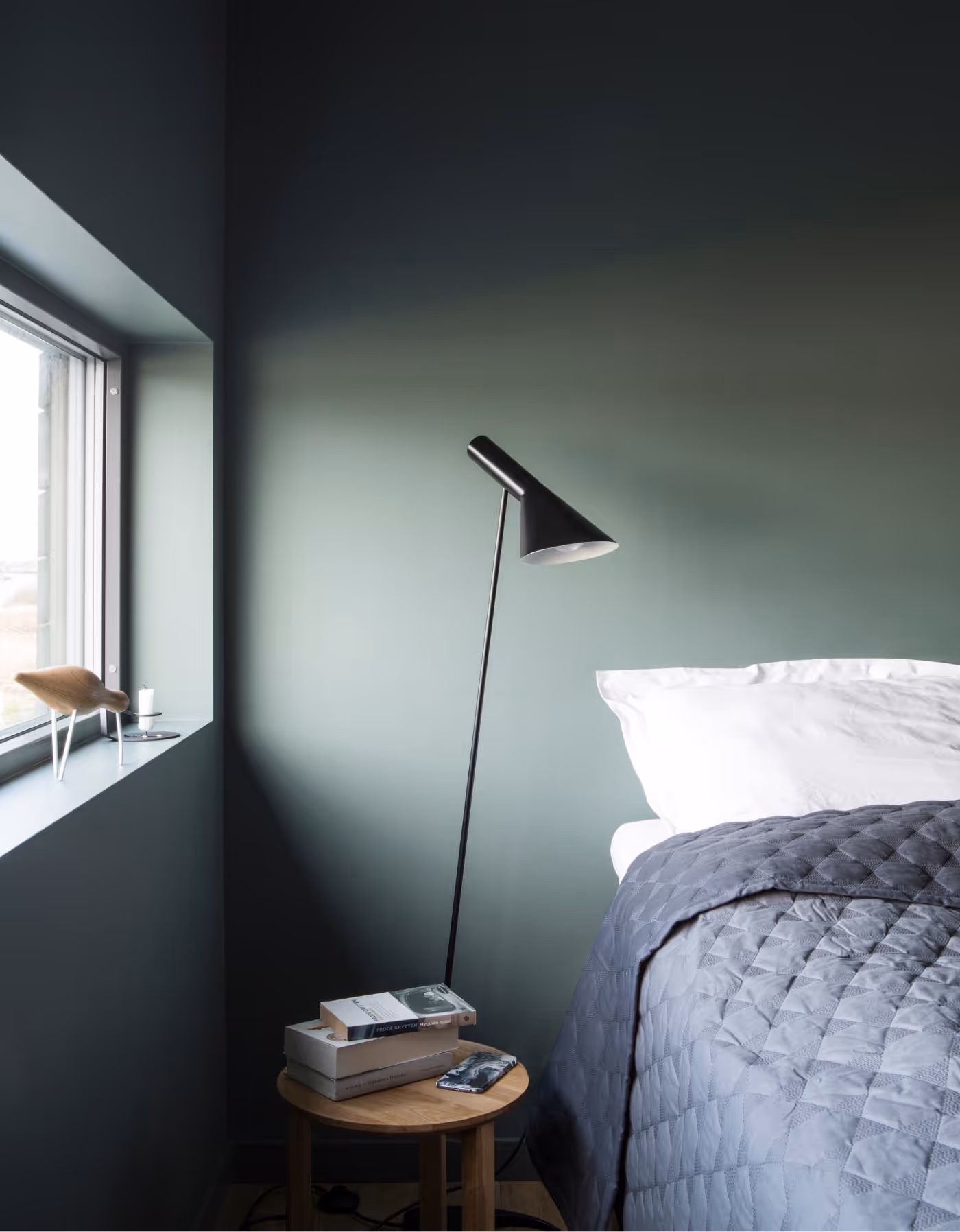 Rolig soverom på Skagenhaugen i Vesterålen med dempet grønn vegg, moderne leselampe og innbydende seng – perfekt for avslappende overnatting i Nord-Norge.