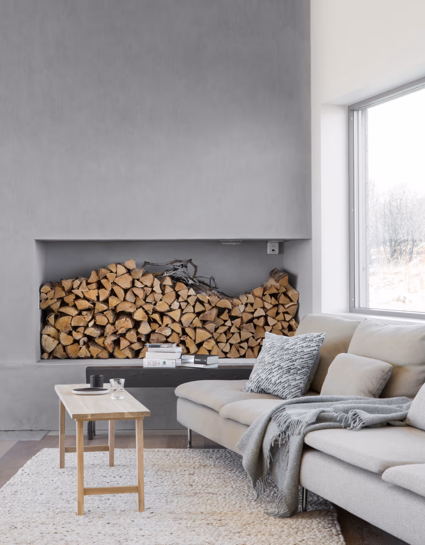 Moderne stue på Skagenhaugen med stor peis, vedstabel og myk sofa – varm atmosfære for avslapning i Vesterålen.