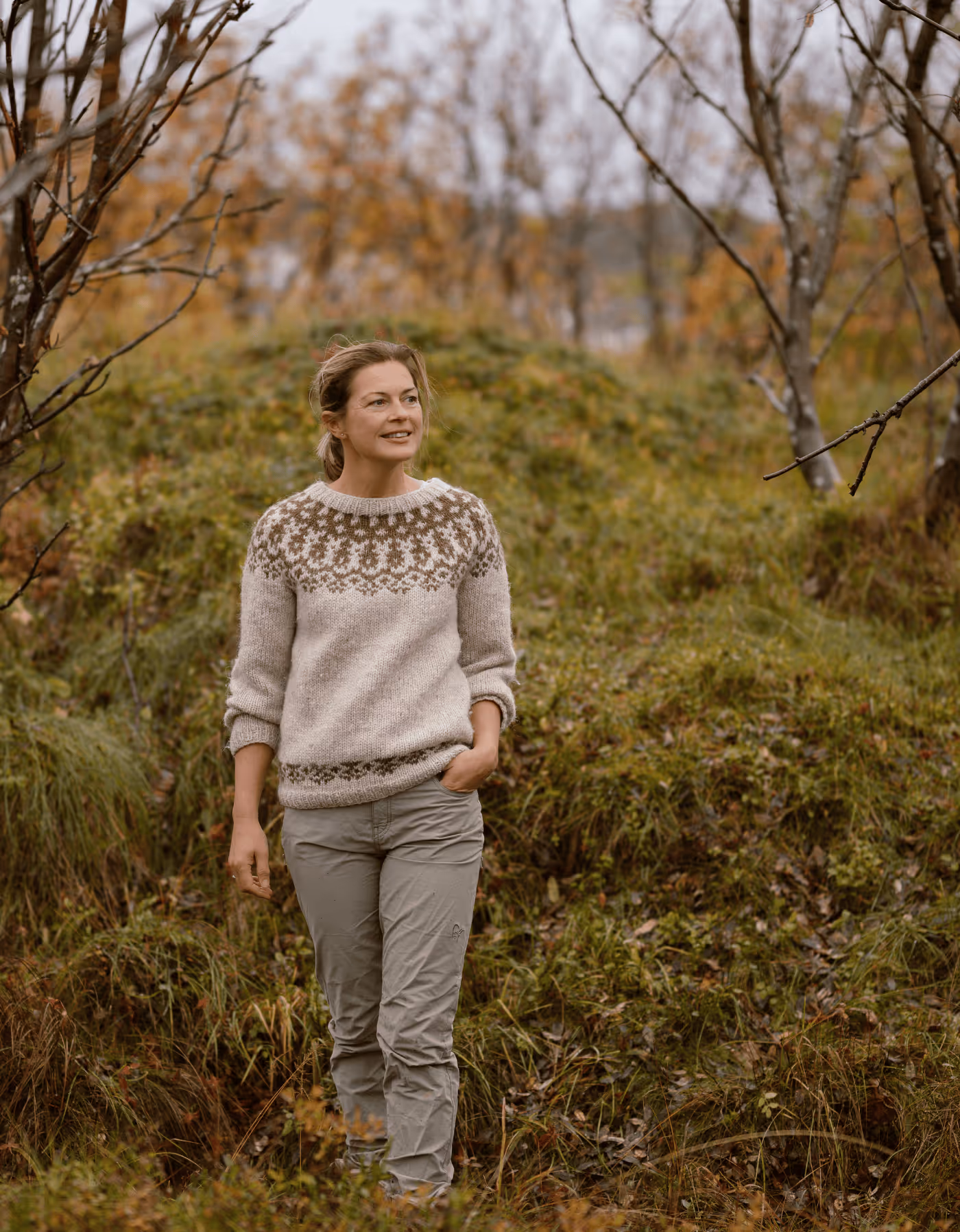 En smilende kvinne i strikkegenser går i nordnorsk natur i Vesterålen 
