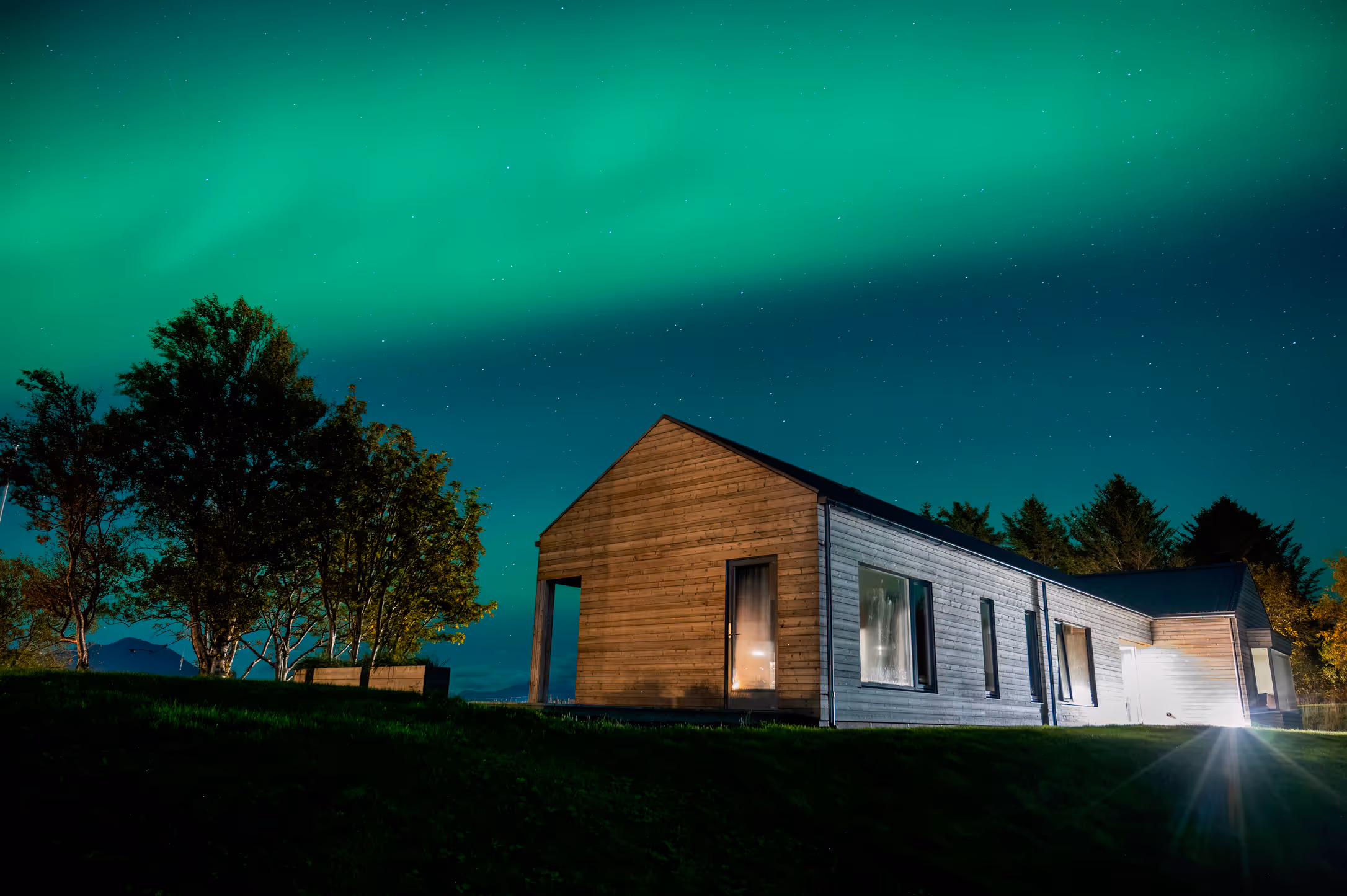 Arkitekttegnet hytte på Skagenhaugen opplyst av nordlys over Vesterålen – et eksklusivt sted for private opplevelser i Nord-Norge.