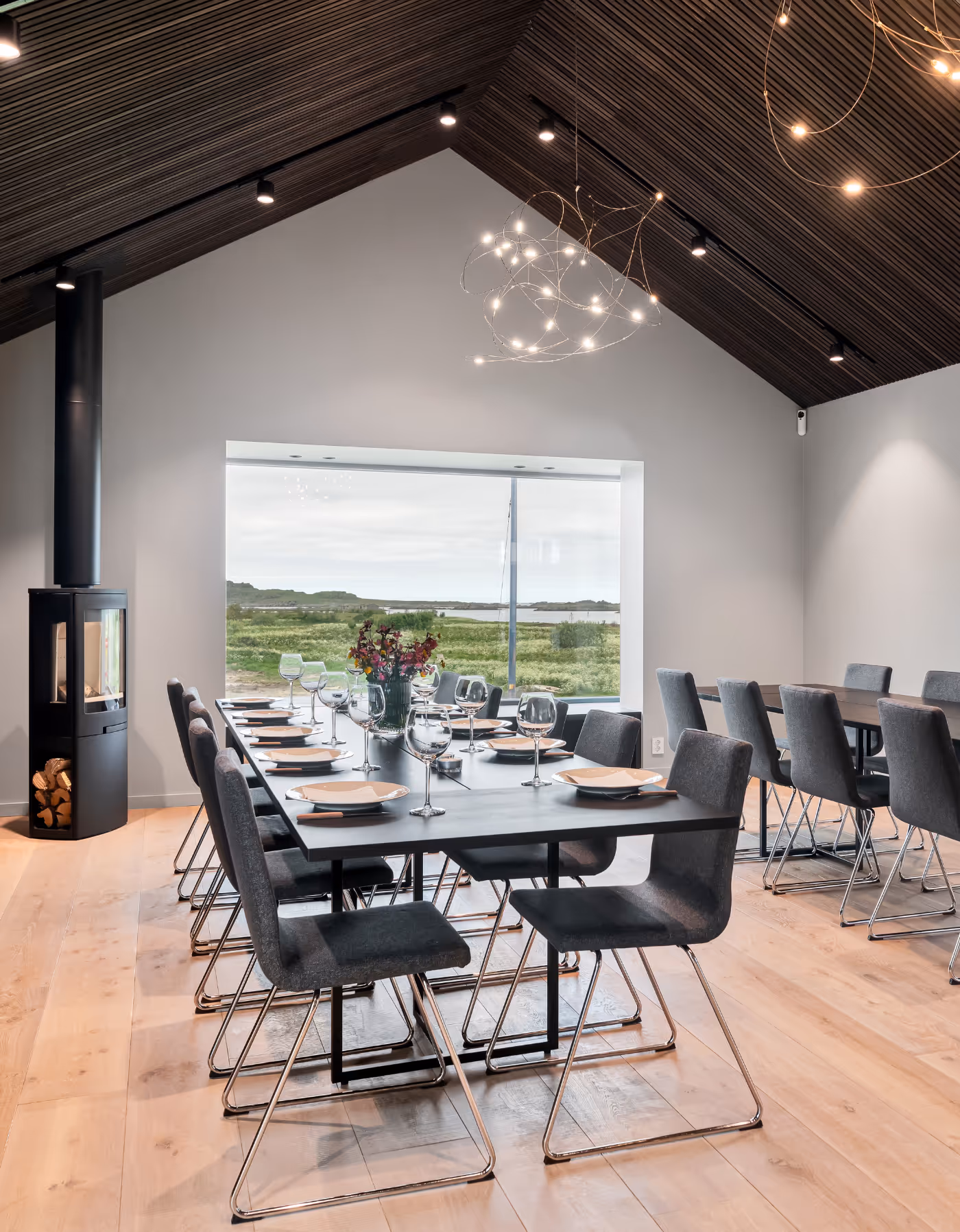 Et stort og luftig møterom med peis, langbord, flere stoler, på dekket og med utsikt over vill nordnorsk natur i Vesterålen