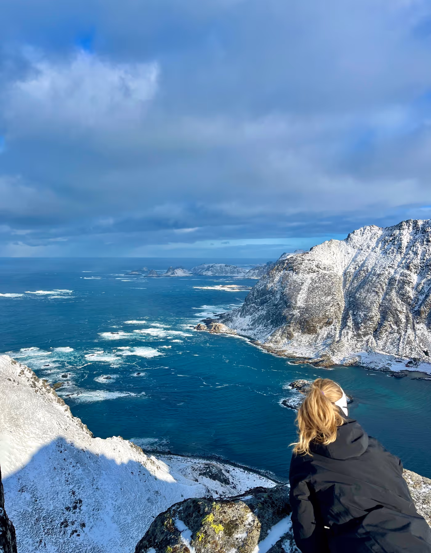 Kvinne ser utover blått hav og snødekte kystfjell i Vesterålen – dramatisk natur ved Skagenhaugen.